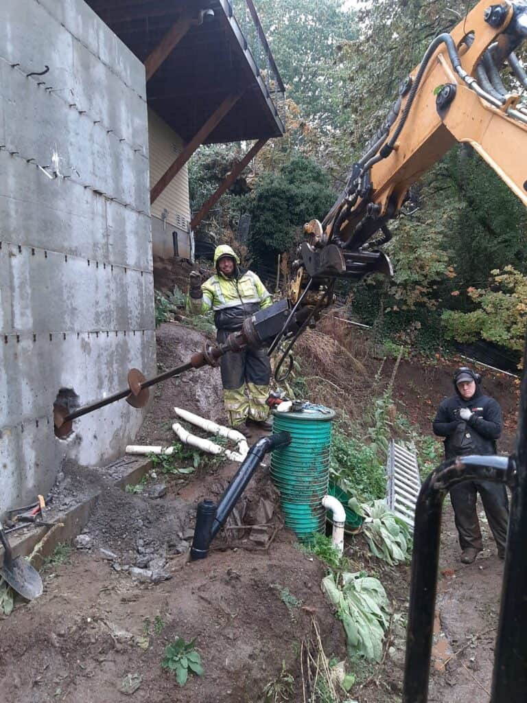 portand-helical-anchor-tieback-foundation-repair TerraFirma technician installing a helical anchor tieback into a concrete retaining wall in Portland OR